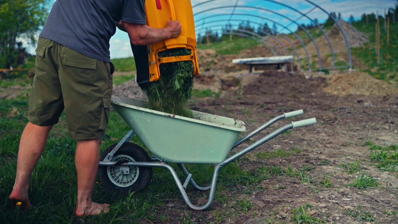Eine metallene Schubkarre, beladen mit gemähtem Gras und Gartenabfällen, die gängige Materialien für Gartenarbeit und Grundstückspflege zeigt