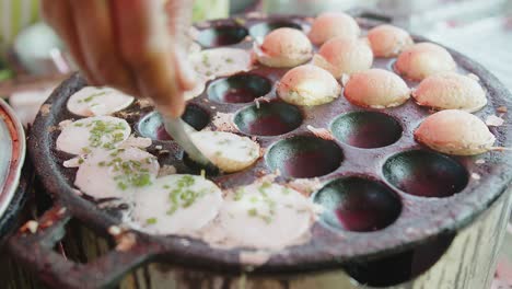 closeup hand cooking traditional thai street food sweet dessert khanom krok on hot pan, coconut milk pancake mix sugar and flour on process with spring onions on top