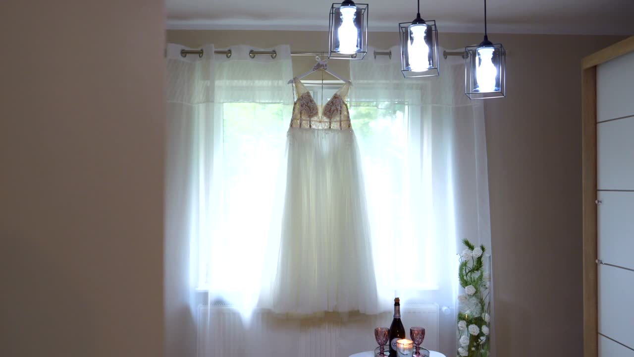 A wedding dress hanging in a salon on a hanger suspended from a window frame