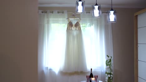 a wedding dress hanging in a salon on a hanger suspended from a window frame