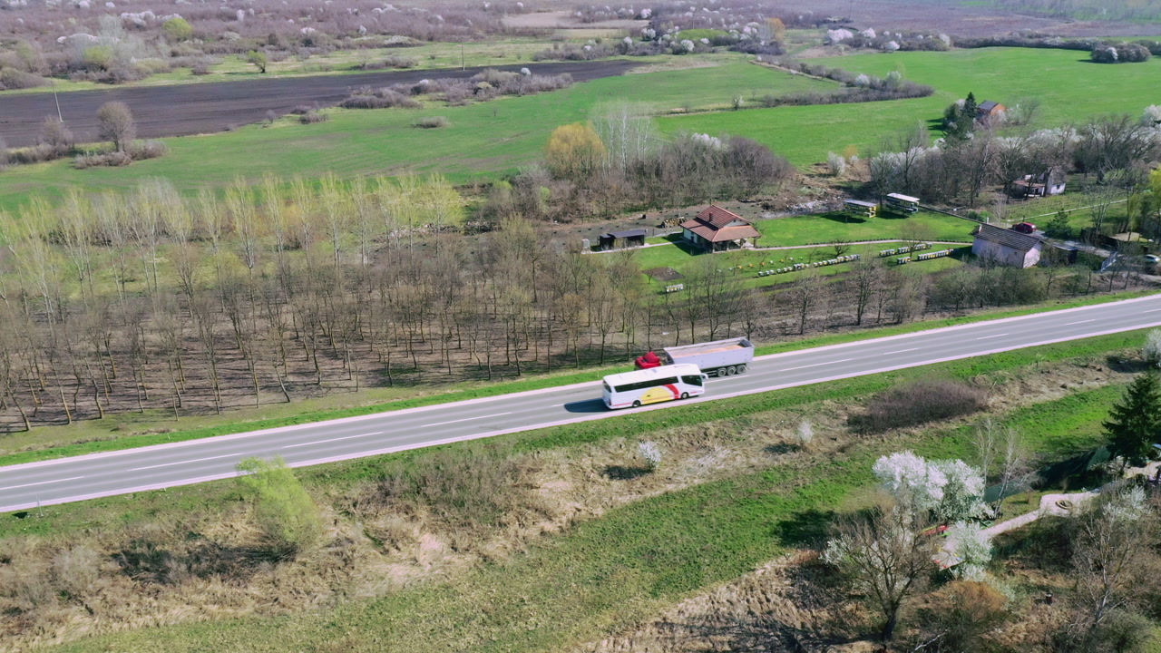 Aerial view of rural road with semi-truck and shuttle bus passing each other, minimal transport scene in dry landscape, 4K drone pov high angle view