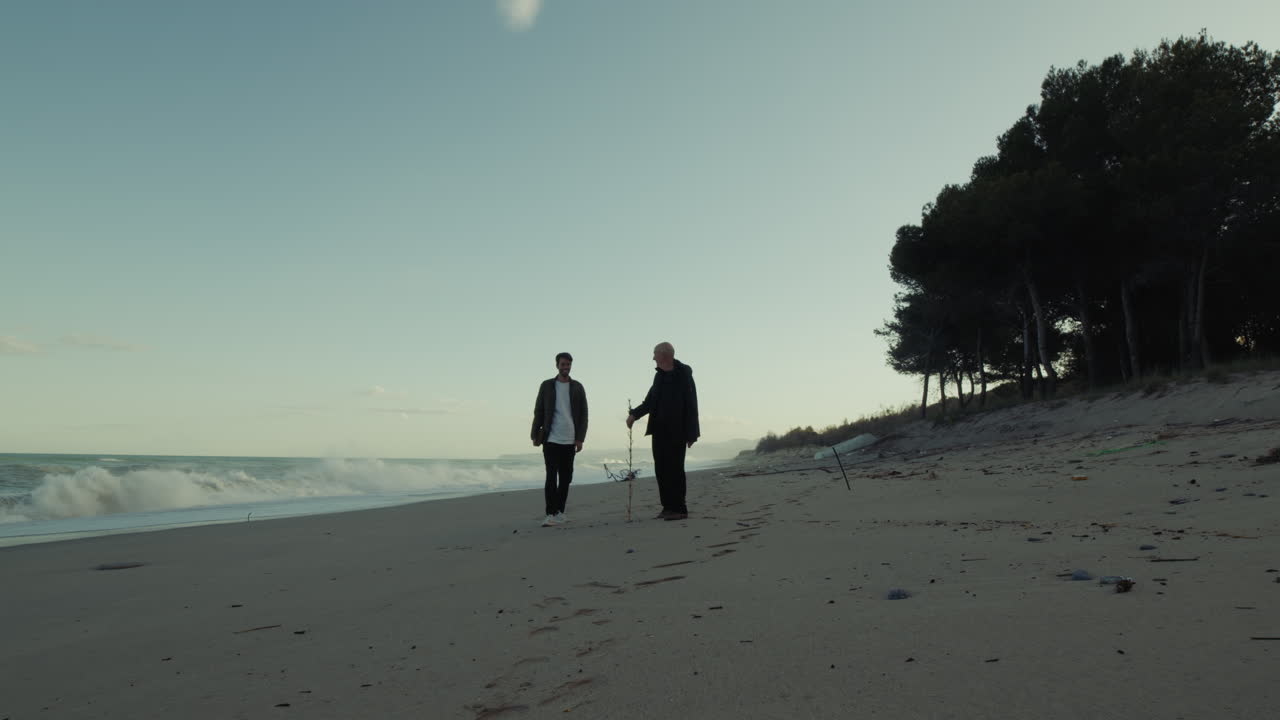 Silhouette Of Senior And Caregiver Walking On Beach At Sunrise Near Ocean