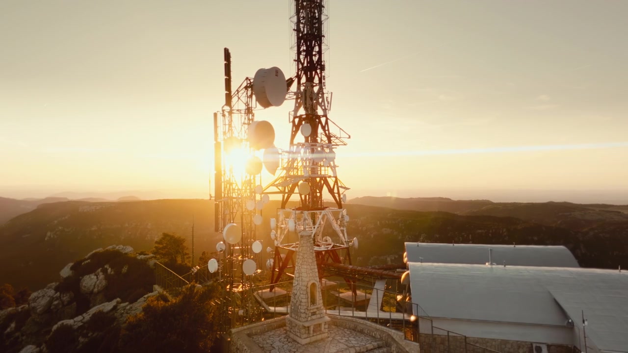 Cinematic 4K drone footage orbiting mountain telecom towers at golden hour. Atmospheric aerial landscape featuring broadcast antennas wilderness and infrastructure.