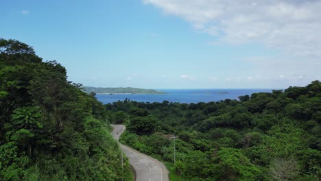 Aerial---Low-rising-drone-of-motorcycle-travel-down-road-near-beautiful-coast