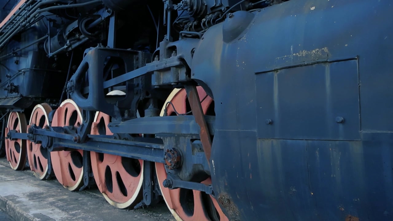 Vídeo mostra as rodas e a lateral de um antigo trem a vapor preto. As rodas são vintage e retrô com coloração vermelha e a filmagem é feita em Tallinn, Estônia, em um local chamado Balti Jaam. Verão, quente.