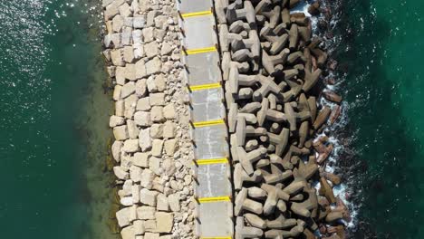 small blue waves from the clear mediterranean sea splash on the man-made pier with large unusually shaped stones on a sunny day in herzeliya israel