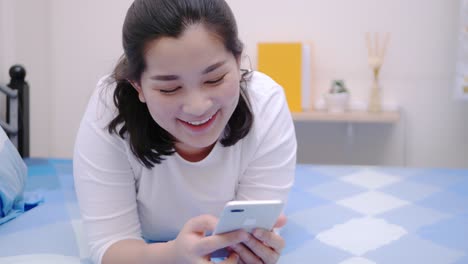 asian woman looking and touching smartphone relax enjoy and smile with online social media in bedroom