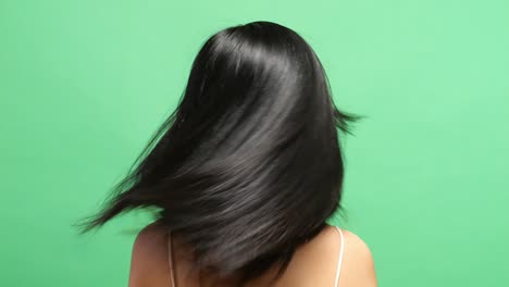 close up back view of a woman shaking her head showing her long black and blond straight healthy hair in the green screen background studio