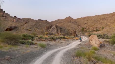 driving in rural road following a motorbike bike rider in desert area off road in wild nature hills and mountain in background in heat hot weather in baluchistan iran outdoor journey travel to nature