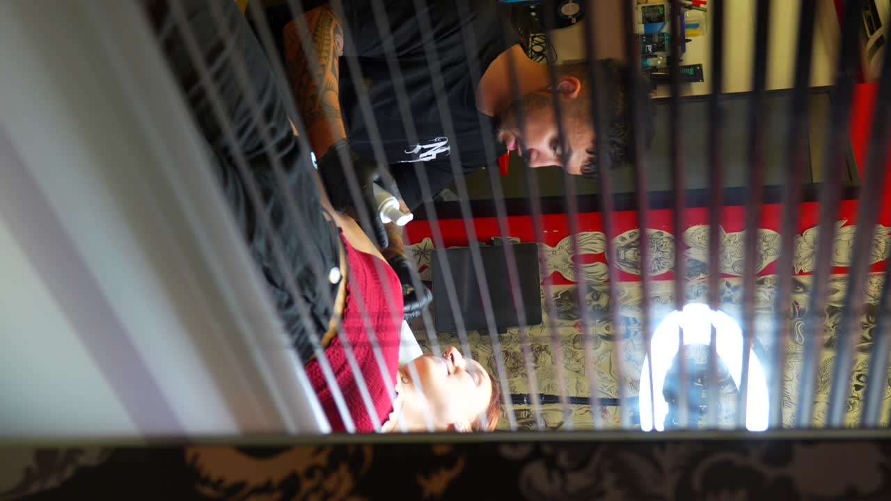 View through a window of a tattoo artist caring for a relaxed female client. Vertical