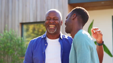 loving senior father with adult son standing outside house laughing together