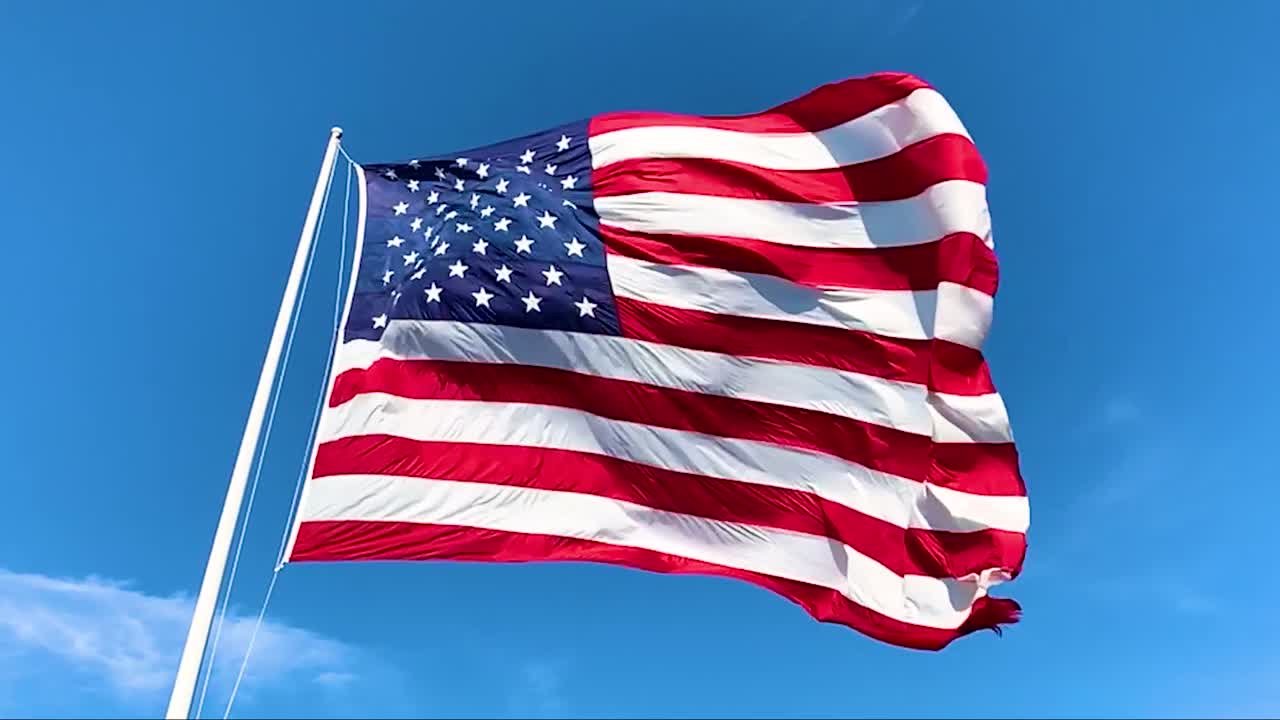 Flag of the United States of America waving in the wind against a blue sky.