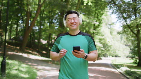 athletic fitness asian sport runner man walking wearing headphones listening music from smartphone