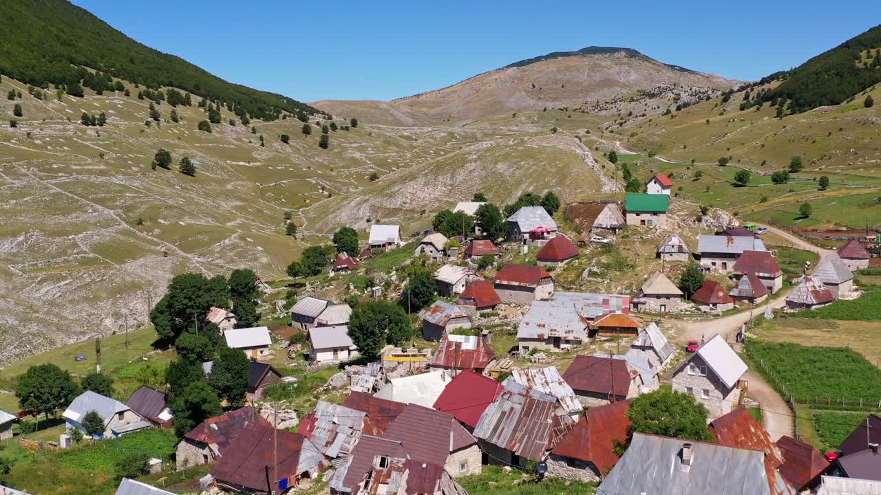 Remote abandoned wooden buildings in green pasture and hillside, aerial approach