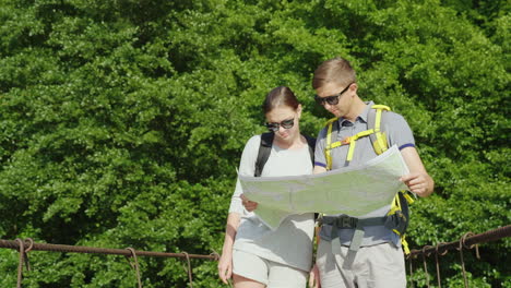 a man and a woman are studying the map they stand on the bridge in the background of a picturesque s