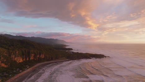 reverse aerial drone view of sunset overlooking pancake rocks on the coastline of punakaiki coastal landscape, west coast of south island, new zealand aotearoa