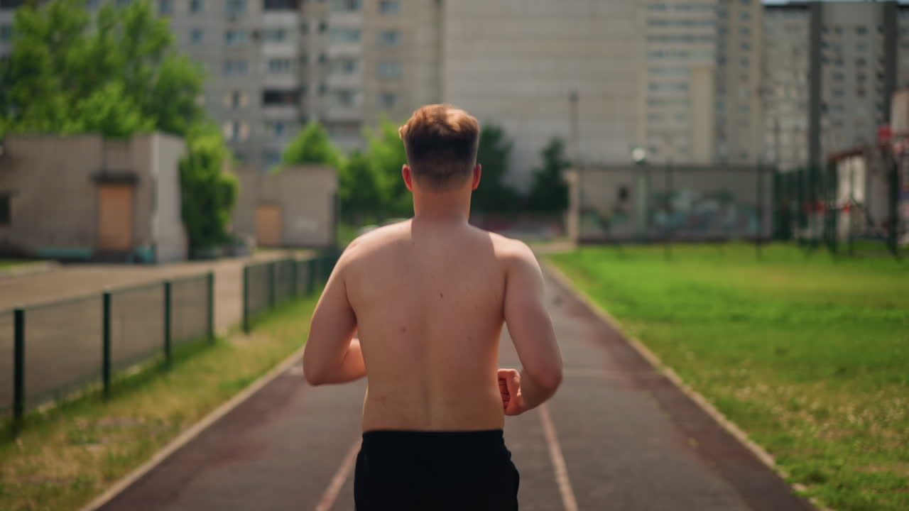 도시 트랙에서 달리는 백인 남성, 아파트 단지에서 보이는 뒷모습, 꾸준한 속도, 여름 햇살, 집중 훈련 세션, 호흡 리듬, 동네 길과 지구력 운동