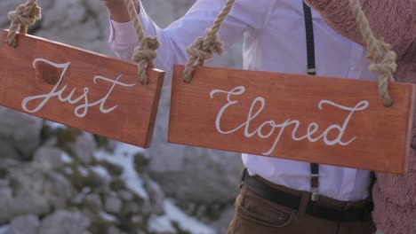 just eloped couple hold wooden sings in hands on mountain elopement, closeup