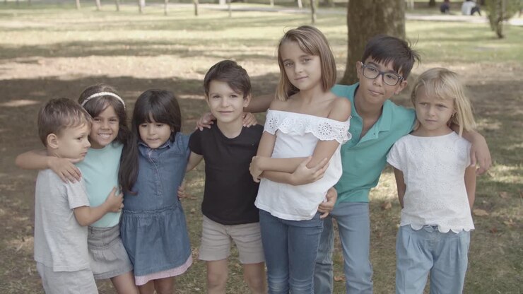 Bambini multietnici in piedi insieme nel parco, che si abbracciano e sorridono alla fotocamera