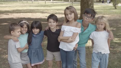 niños multiétnicos parados juntos en el parque, abrazándose y sonriendo a la cámara