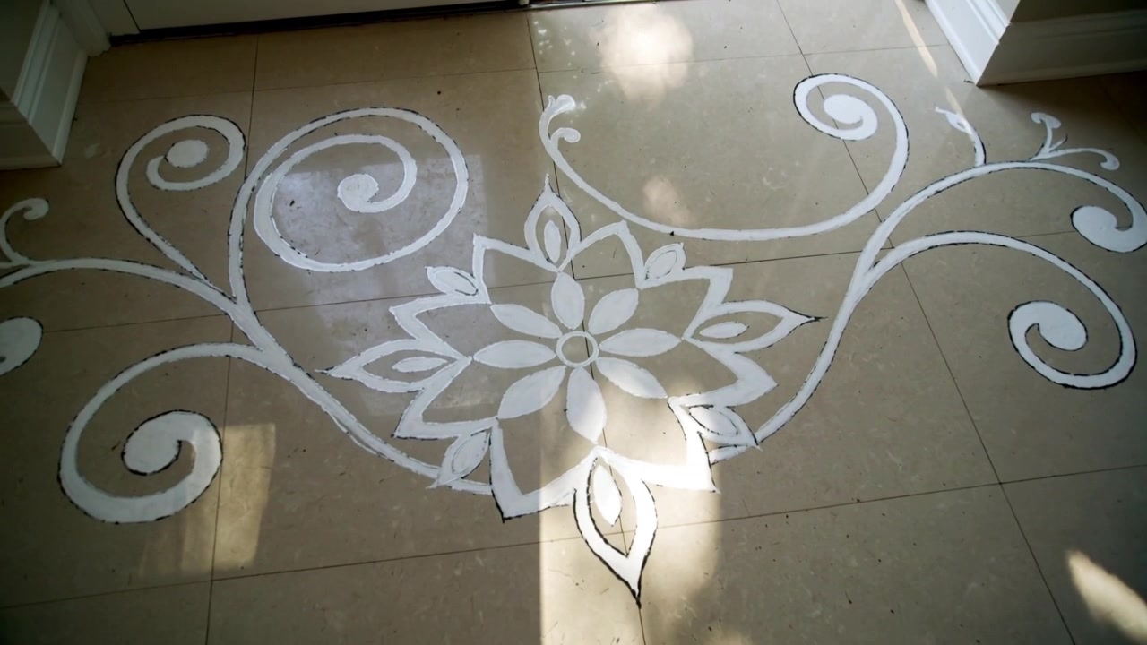 Spostamento della telecamera che rivela un mandala bianco su un pavimento d'ingresso piastrellato vicino a una porta, con ombre di foglie in movimento.
