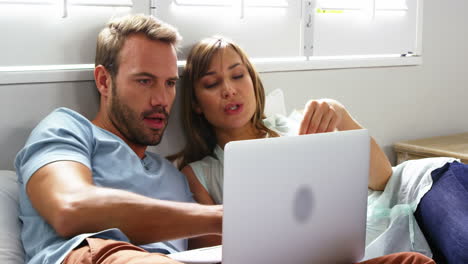 pareja feliz acostada en la cama haciendo compras por internet
