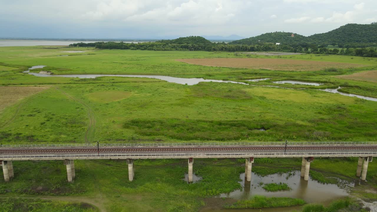 흐린 오후 동안 고가 철도, 농지, 수로, 언덕 및 호수를 보여주는 왼쪽으로 미끄러지는 항공 영상