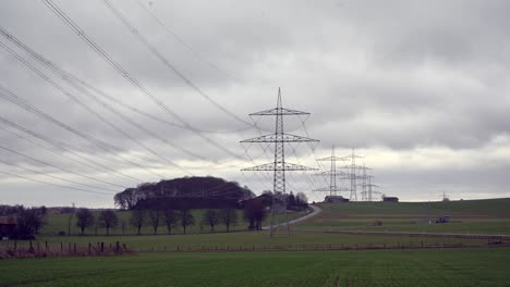 llevar energía a la gente: lapso de tiempo de las líneas de transmisión eléctrica en un cielo nublado sobre campos verdes