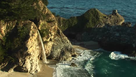 birdseye shot of a waterfall crashing down into a secluded pool of the california pacific ocean 1