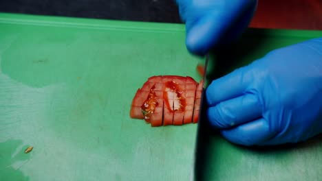 Chef-with-gloves-quickly-cutting-tomato-slice-on-a-table,-push-in