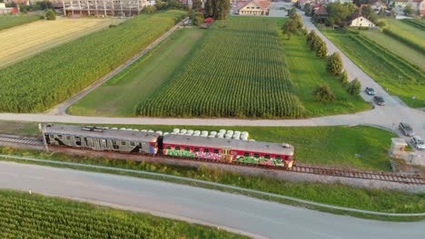 train passes rural railway crossing, farm fields, distant town, aerial