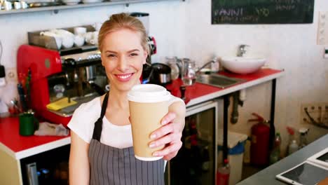 Retrato-De-Una-Camarera-Sonriente-Ofreciendo-Una-Taza-De-Café-En-El-Mostrador