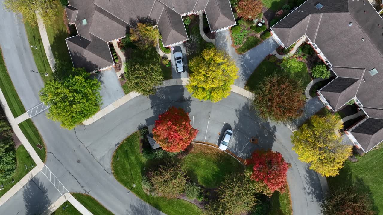 Multicolored trees in noble suburb neighborhood witch villas on sunny autumn day. Aerial top down circle shot. Large properties and parking cars in quiet suburbia of USA