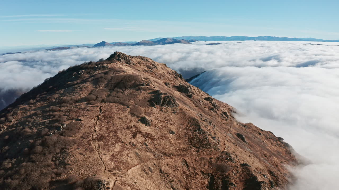 pico de la montaña que se eleva sobre un mar de nubes bajo cielos azules claros, amplia toma aérea