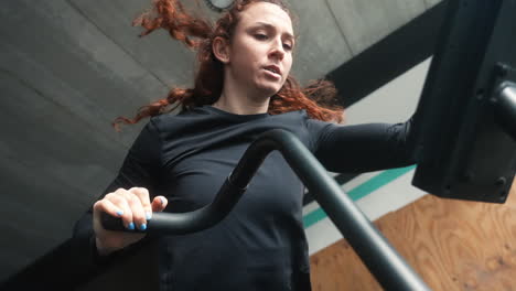 red-haired woman's intense crossfit training on an air bike in a close-up, slow-motion shot