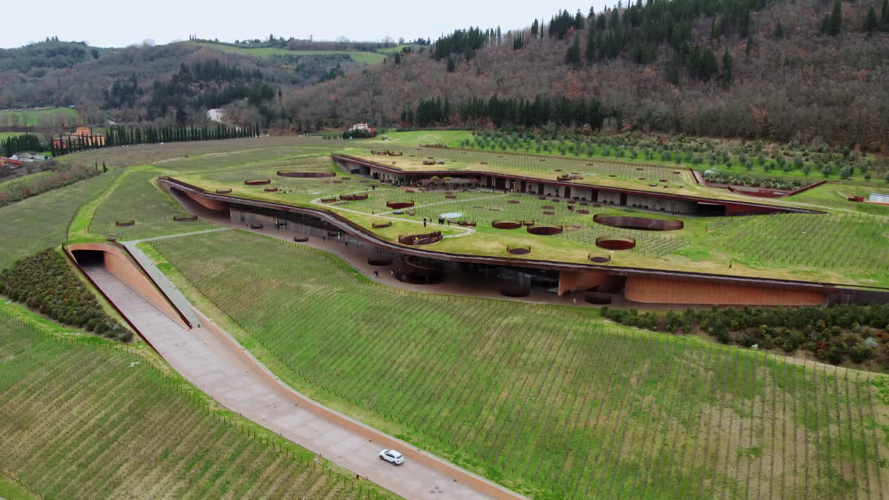 Flying Around a Cutting-Edge Winery in the Rolling Hills of Tuscany with a car passing on the road entering the tunnel