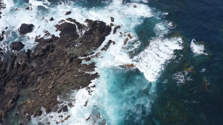 Volo sopra onde blu azzurro che si infrangono sulle aspre scogliere costiere delle Isole Canarie.