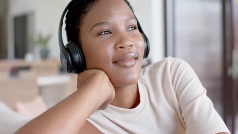 Happy-african-american-woman-sitting-on-sofa-using-headphones-and-listening-to-music,-slow-motion