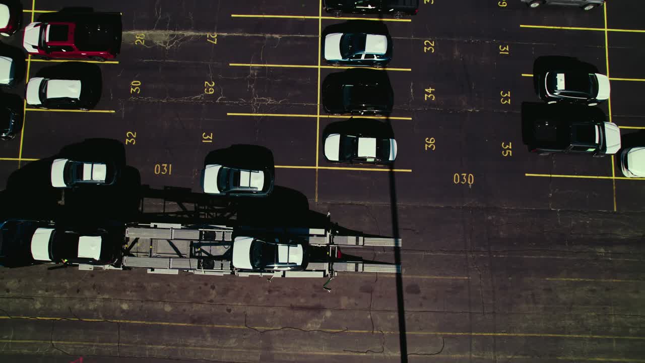 A car transport truck being loaded on a huge parking lot, seen from above.