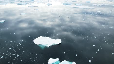 sky reflecting on calm ocean water with icebergs floating, aerial view