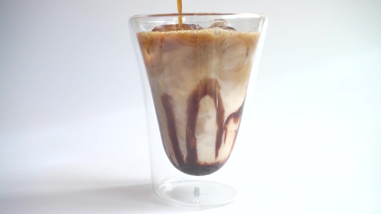 Preparación de bebida de café con hielo, leche, café y sirope de chocolate. Cámara lenta.