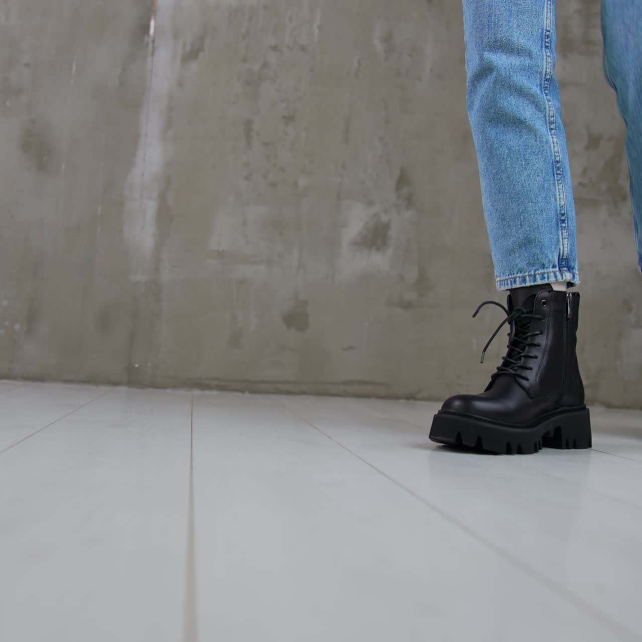 Stylish black leather low boots with laces on a lady. Close up. Model wearing jeans walks by the studio showing her modern footwear