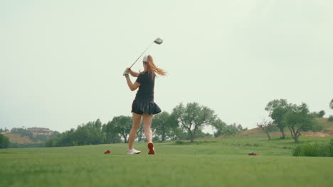 a female golfer unleashes a powerful drive off the tee, filmed from a dramatic ground-level angle. the low perspective highlights her athletic swing and energy against the open course landscape.