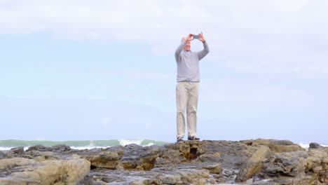 front view of old caucasian senior man clicking photo with mobile phone at beach 4k