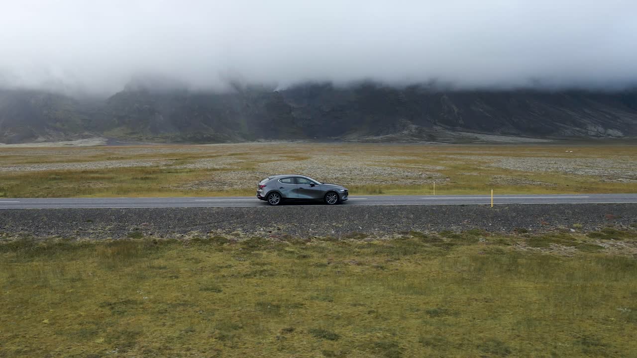 Traverse Iceland's scenic expanses with this captivating 4K drone footage, featuring a unique arial view as a car drives through the bare countryside of Iceland