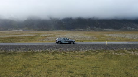 Traverse-Iceland's-scenic-expanses-with-this-captivating-4K-drone-footage,-featuring-a-unique-arial-view-as-a-car-drives-through-the-bare-countryside-of-Iceland