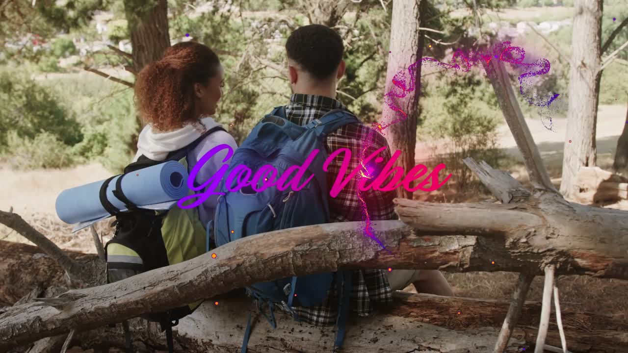 Dvojice turistů sedí venku na kládě, poté co žena promluví, prolínají se částice představující „Good Vibes“.