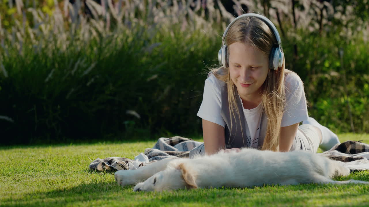 십대 소녀는 강아지와 함께 놀고, 잔디에 누워서 헤드폰으로 음악을 듣습니다.