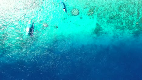 Traditional-Balinese-boats-anchoring-on-blue-turquoise-seawater-over-beautiful-sea-bottom-with-rocks-and-pebbles