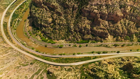 Narrow river flowing at the foot of a mountain. Two highways going by the waterfront of the river in Colorado, USA. Aerial view.